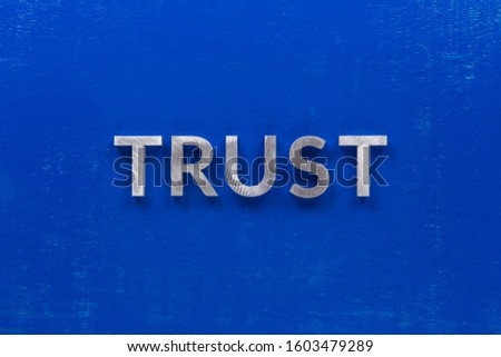the word trust laid with silver metal characters on blue painted wooden board in central flat lay composition