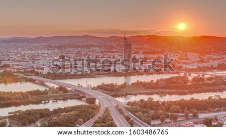 Aerial panoramic view of sunset over Vienna city with skyscrapers, highway intersection and a riverside promenade timelapse in Austria. Evening skyline from Danube Tower viewpoint