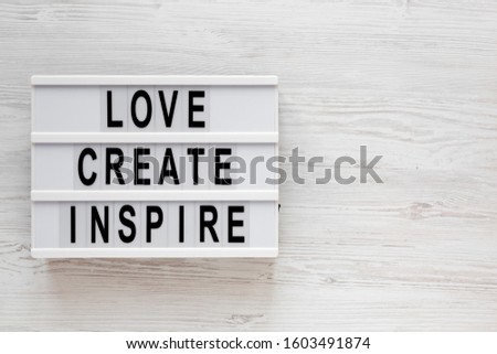 'Love create inspire' words on a lightbox on a white wooden background, top view. Overhead, from above, flat lay. Space for text.