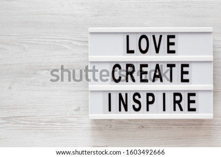 'Love create inspire' words on a modern board on a white wooden surface, top view. Overhead, from above, flat lay. Copy space.