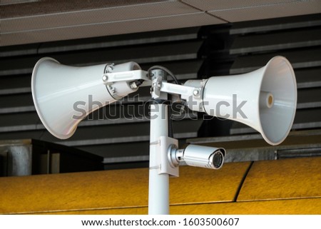 two white loudspeakers and security camera on pole in a public place. providing security in the city, notification of emergencies, informing passengers, technical means of notification and Royalty-Free Stock Photo #1603500607