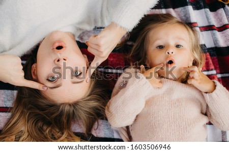 Wondered emotional amazed young woman and child playing and posing on camera together. Luing on red striped blanket. Pointing on eyes and mouth