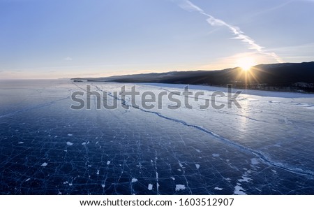 Frozen Lake Baikal, Lake Baikal hummocks. Beautiful winter landscape with clear smooth ice near rocky shore. The famous natural landmark Russia. Blue transparent ice with deep cracks. Royalty-Free Stock Photo #1603512907