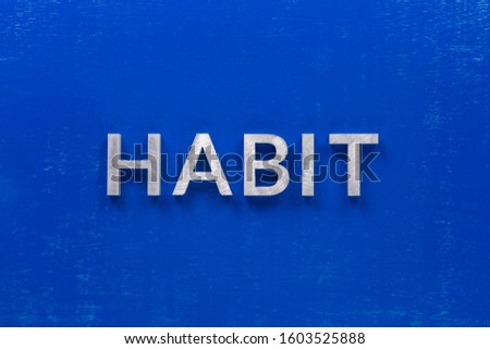 the word habit laid with silver metal characters on blue painted wooden board in central flat lay composition