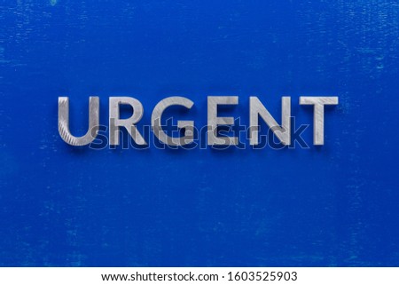 the word urgent laid with silver metal characters on blue painted wooden board in central flat lay composition