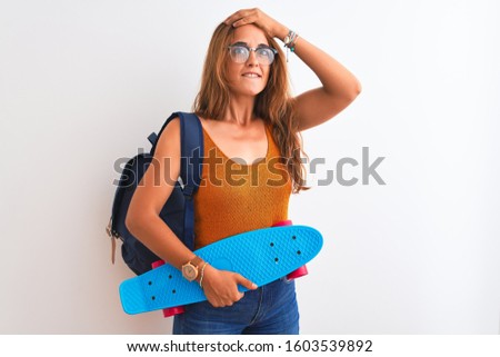 Young redhead student woman wearing backpack and skateboard over isolated background stressed with hand on head, shocked with shame and surprise face, angry and frustrated. Fear and upset for mistake.