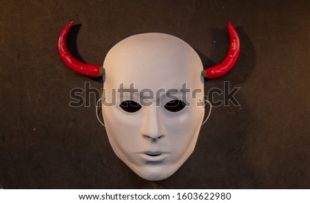 white mask with horns of red peppers on a black background