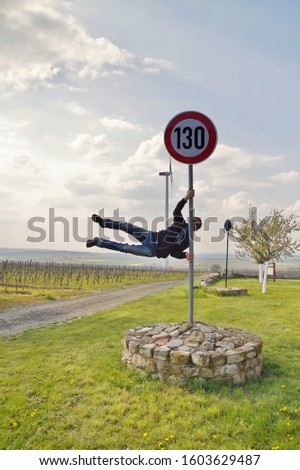 130 kmph or mph driving speed limit sign. strong pole dancer man in street clothes on pylon. athletic man doing human flag exercise outdoor. mast with German 130 speed limit sign. road safety concept