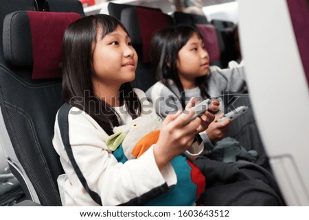 Adorable little Asian girls traveling by an airplane. Children sitting by aircraft watching movie during the flight. Family traveling abroad with kids.