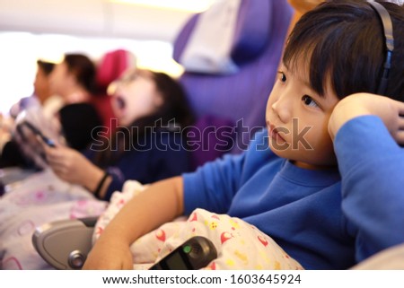 Cute little Asian boy traveling by an airplane. Children sitting by aircraft watching movie during the flight. Family traveling abroad with kids.