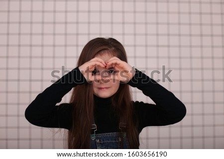 young smiling girl of eight years with long hair in a black turtleneck and denim sundress on a white background in a black cage in a good mood different emotions