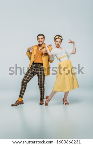 cheerful dancers looking at camera while dancing boogie-woogie on grey background