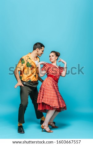 cheerful dancers looking at each other while dancing boogie-woogie on blue background