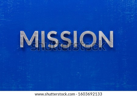 the word mission laid with silver metal characters on blue painted wooden board in central flat lay composition