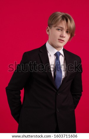 Young teenager guy in a black jacket and tie posing on a red background