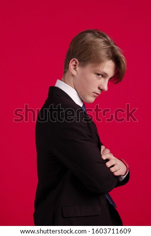 Young teenager guy in a black jacket and tie posing on a red background