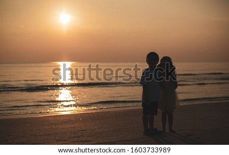 Silhouette of two children standing on the beach while turn back from sunset view, Travel lifestyle, summer vacation with kids, copy space for text