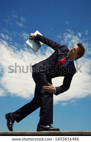 Businessman crouching in position to throw a laptop computer like a discus in a track and field event