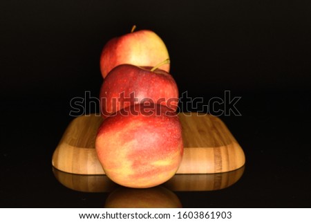Three whole red ripe juicy sweet apple on a brown wooden tray, on a black background.