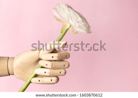Wooden hand with a white flower on a pink background copyspace side view