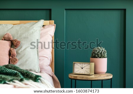 Stylish bedroom interior with design coffee table, plant, gold clock and elegant personal accessories. Beautiful bed sheets, blanket and pillows. Template. Modern home staging. Wall panelling. Details Royalty-Free Stock Photo #1603874173