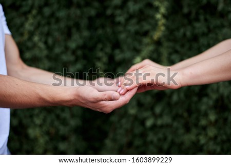 Arms of young couple in love, embracing. Close-up picture of romantic couple hands holding together in front of green leaves wall in summer. Romantic relationship. Valentines day