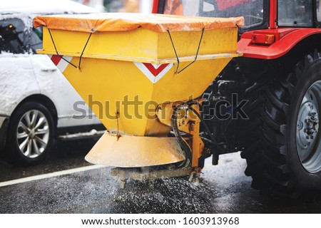 Tractor with mounted salt spreader, road maintenance - winter gritter vehicle.  Tractor de-icing street, spreading salt. Municipal service melting ice on streets. Diffuser of salt blend on road