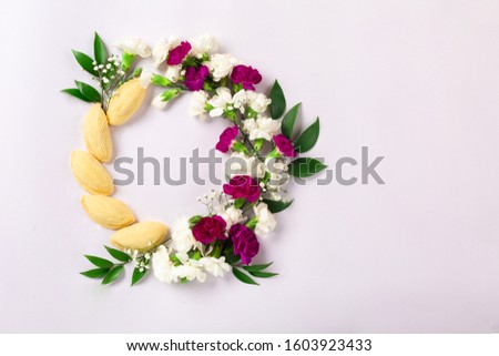 Novruz wreath made of traditional Azerbaijan pastry shekerbura and beautiful white, violet flowers for spring celebration, light lilac background, top view. Translation: "Happy Nowruz" greeting card