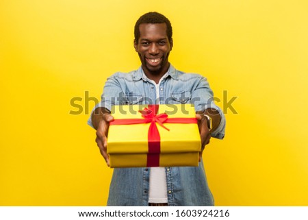 This present for you! Portrait of happy generous man in denim casual shirt giving wrapped gift box and smiling at camera, congratulating on birthday. indoor studio shot isolated on yellow background