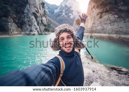 Happy traveller man takes a selfie photo on a lake at the mountain 