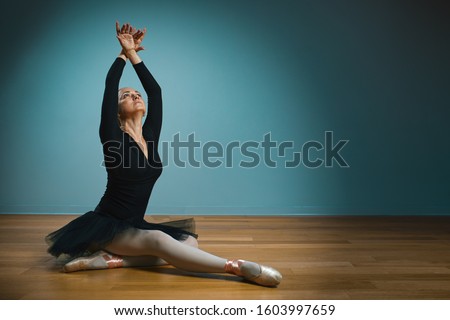 pretty woman ballerina in tutu and pointe in black swimsuit posing in studio on blue background
