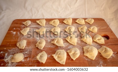 Homemade pelmeni, Russian traditional dumplings on a wooden cutting board with flour and ingredients for homemade. Process of making pelmeni, ravioli or dumplings with meat