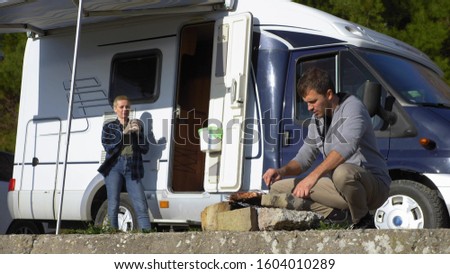 a man cooks meat on the grill outdoors on a background of motorhomes.