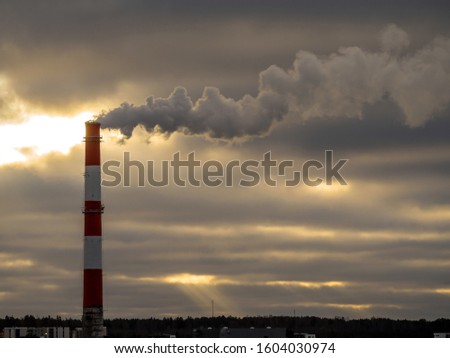 Stock Photo - Big industrial red and white pipe with smoke going outside. Toxic smoke pollutes the atmosphere. Factory pipe polluting air, environmental problems. Dark clouds on the background. Toning