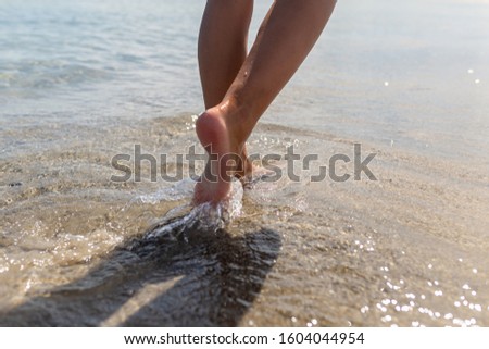 Beautiful tanned legs of a girl walking in the water. The girl runs through the sea water on the edge of the beach.