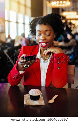 Portrait of a smiling woman sitting in a cafe taking a cell phone picture of her cupcake