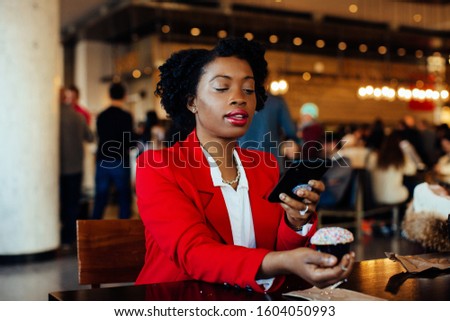 Portrait of a young woman sitting in a cafe taking a cell phone picture of her cupcake