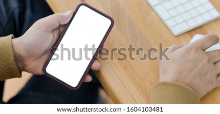 Close-up view of young man holding blank screen smartphone in comfortable office room 