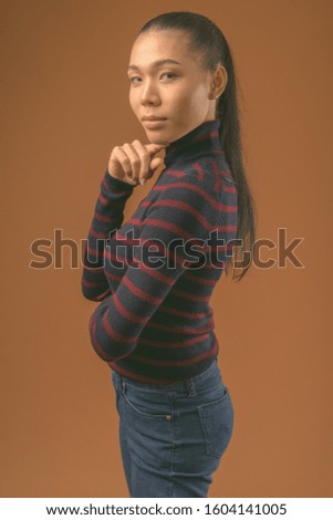 Young beautiful Asian transgender woman against brown background