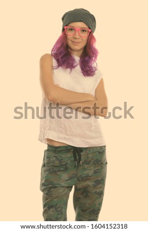 Studio shot of young beautiful woman standing and wearing pink eyeglasses with arms crossed