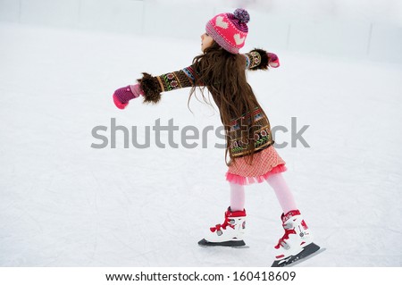 Adorable little girl in winter clothes and bobble hat skating on ice rink