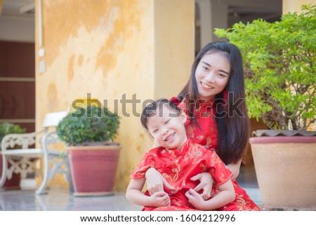 Little asian girl and her mother in chinese traditional costume sitting in front of their home and smiling happily in Chinese new year festival.