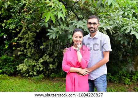 Indian husband holding Asian wife on festive season.People celebrating Chinese New Year.Man with beard.Female with pink dress.Multiracial Malaysian couple. Greeting in the outdoor.