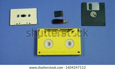 Evolution of memory storage devices, from VHS Tape and Audio Cassette, Film, Floppy disk to USB flash stick and SD memory card. blue retro background 