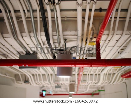 Picture of red fire fighting pipe system and electrical system pipe hanging from concrete ceilings in the building