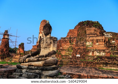 ancient big Buddha statue in front of damaged brick pagoda on blue sky background, Ayutthaya Thailand