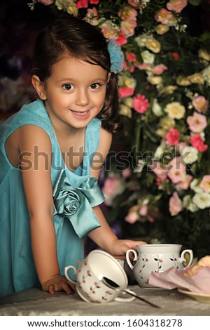 Beautiful Little girl in a smart dress around the table with tea and marshmallow