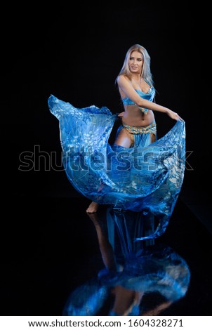 Young woman belly dancer in a blue oriental costume on a black background