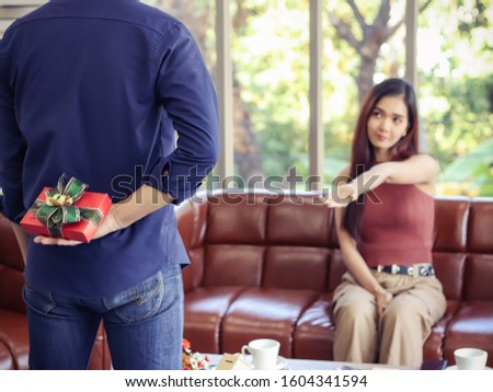 Blur image of woman siiting on couch in living room , looking at her boyfriend open her palm asking for present the her boyfriend hiding back , selective focus on gift box.