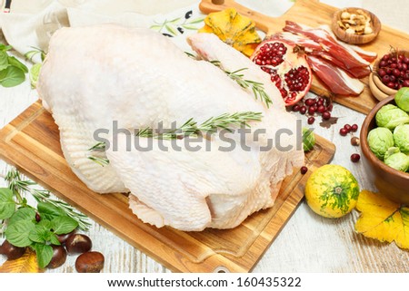 Whole raw  turkey on wooden cutting board with vegetables, ham and  spices.Preparing Thanksgiving Dinner with Turkey  and ingredients such as  bacon, vegetables, nuts, cranberries, pomegranate, spices